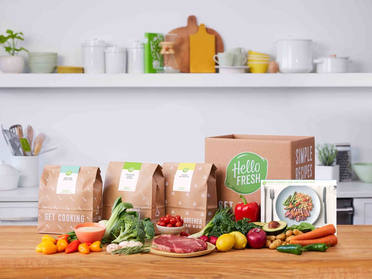 Branded HelloFresh meal-kit box with labeled pre-portioned ingredient bags, fresh produce, and a recipe card on a kitchen counter